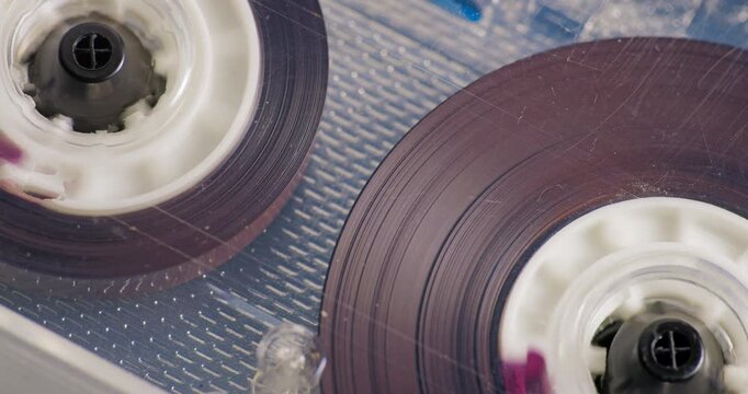 Extreme close-up of transparent audio cassette. Audio Cassette Fast Rewind. Transparent compact cassette with brown tape rewinding at high speed.