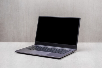 Fototapeta premium laptop on a gray table with a black mockup on the screen on a gray background close-up