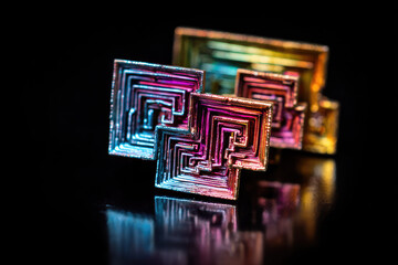 Iridescent bismuth crystal structure showing geometric spiral pattern and metallic rainbow color reflecting on black background with mesmerizing intricate texture and shiny surface