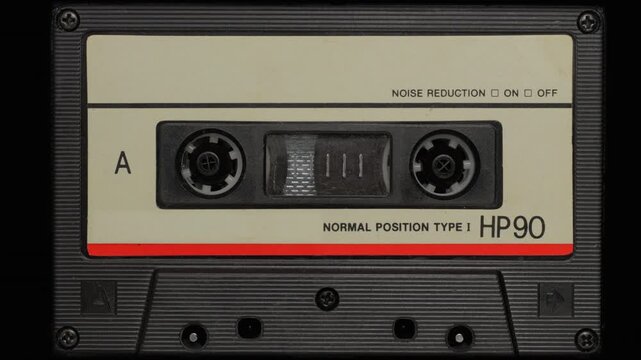 Audio Cassette Reels Spinning. Retro compact cassette tape with spinning reels on black background.	
