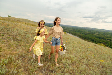 Family on a meadow, mother and daughter holding hands while carries picnic basket