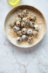 Beige bowl with uncooked quail eggs on a white stone background, vertical shot with space, flat lay