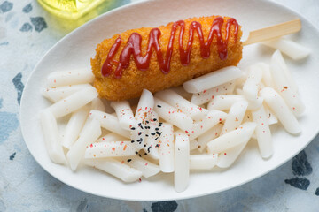 Tteokbokki or korean traditional rice cakes served with a corn-dog on a white plate, horizontal shot, middle closeup