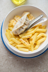 Bowl with cheesy korean tteokbokki or rice cakes, steamed egg and dumpling, vertical shot on a beige stone background, middle close-up