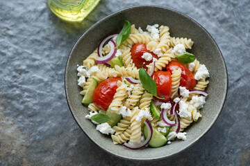 Bowl of pasta salad with fusilli on a dark-grey granite background, horizontal shot, high angle view