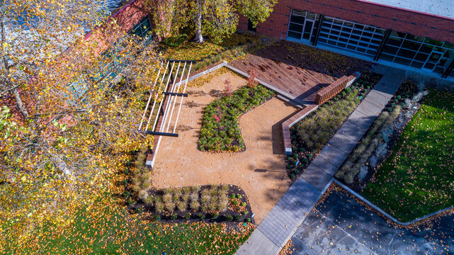 Aerial view of a garden space with a wooden deck, gravel paths, and linear pergola, contrasting with the surrounding autumn foliage, Apollo Park, Oregon, United States.