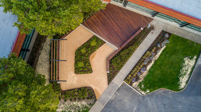Aerial view of a modern landscape design featuring a wooden deck, winding gravel paths, and vibrant green lawns and trees, Apollo Park, Oregon, United States.