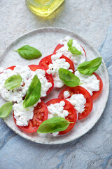 Cottage cheese caprese with ripe tomatoes and green basil, vertical shot on a beige and blue stone background, high angle view
