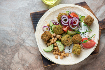 Flat bread with falafel, yogurt, chickpeas and fresh vegetables, horizontal shot on a brown granite background, elevated view