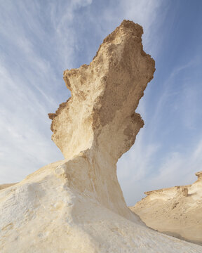 View of a dramatic, wind-sculpted limestone rock formation rises against a pale blue sky, showcasing nature's artistry, Zekreet, Al Sheehaniya Municipality, Qatar.