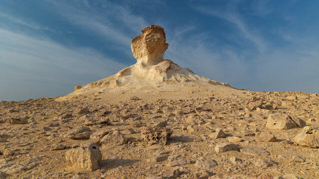 View of stark, sun-baked limestone formations rise from the arid desert landscape under a vast sky, creating a surreal vista in Zekreet, Al Sheehaniya Municipality, Qatar.