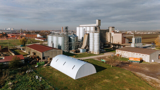 Aerial view of a grain processing plant gleams with metallic silos against a backdrop of industrial buildings and autumn-tinted trees, Sremska Mitrovica, Vojvodina, Serbia.