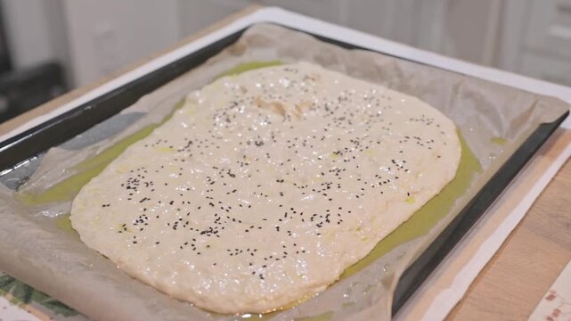 Baking foccacia by amateur. Hands dimpling and drizzling olive oil over shaped. Focaccia baking tutorial. Highlighting bubbly surface formation before baking. Authentic home cooking visuals.