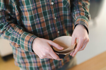 A person in a plaid shirt prepares to brew coffee. They are holding a filter cone and carefully placing a paper filter inside it. This shows the pour-over coffee making process.