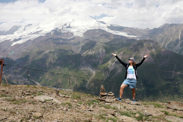 Woman stands with arms outstretched at Mount Cheget with snowy mountains background