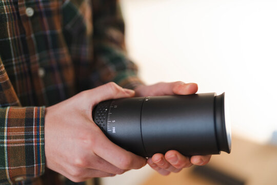 A person in a plaid shirt holds a black cylindrical coffee grinder. They are adjusting the grind setting, indicated by the "FINE" marking and numbers. This shows a focus on precision.