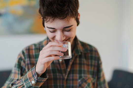 A smiling young person in a plaid shirt holds a small clear container of ground coffee. They close their eyes, deeply inhaling and enjoying the rich aroma.