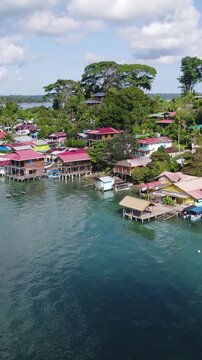 Vertical aerial view showcasing colorful houses along the coast of Bastimentos Island, Panama, with lush greenery and clear blue waters.