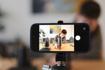 A smartphone on a tripod records a young person preparing coffee. The individual is grinding fresh coffee beans, creating content for a video or photo shoot.