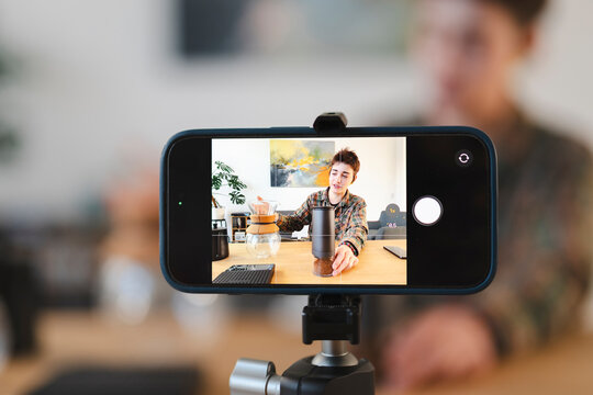 A young content creator films a coffee tutorial with a smartphone on a tripod. They showcase a coffee grinder and pour-over brewing method for their audience.