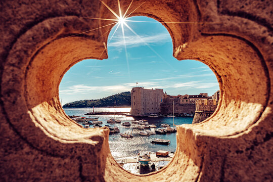 View of the sun's rays sparkle over the ancient harbor, framed by the stone architecture, where boats bob gently on the azure waters, Dubrovnik, Dubrovnik-Neretva County, Croatia.