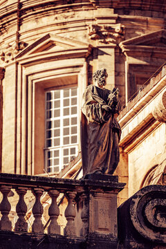 View of an aged statue poised on a stone balustrade against the backdrop of an ornate, sun-drenched building, Dubrovnik, Dubrovnik-Neretva County, Croatia.