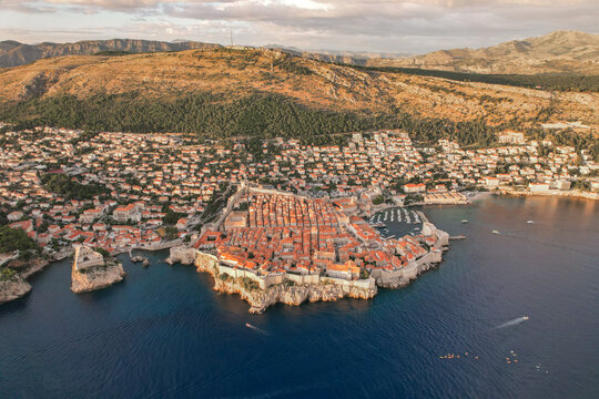 Aerial view of terracotta rooftops cascading down to meet the azure Adriatic Sea, cradling the ancient walls of Dubrovnik, Croatia.