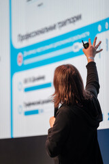 Presenter stands before large screen showcasing charts during conference, pointing with laser device, engaging audience and sharing insights.