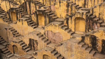 view of the ancient Chand Baori stepwell's geometric patterns and symmetrical staircases descend into the earth, creating a mesmerizing architectural marvel, Abhaneri, Rajasthan, India.