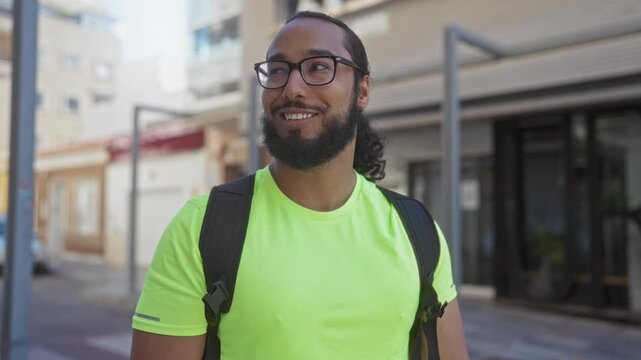 Man with backpack and glasses smiling and looking to side on a city street in neon green shirt and beard; urban optimism exploration.