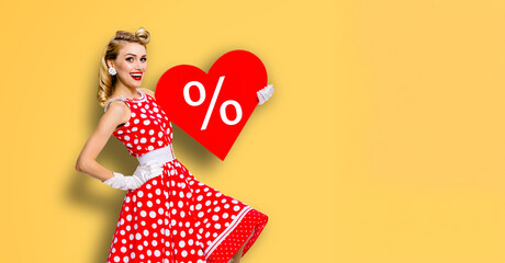 Expressive smile pinup beautiful cute woman point red heart paper banner with percentage percent % discount sign. Pin up girl. Retro concept. Isolate orange yellow background. Valentine or like symbol