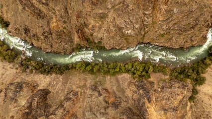 A river flows through a canyon surrounded by rocky cliffs and sparse vegetation © Михаил Уванов
