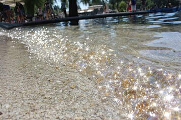 Shallow water sparkles near a pebbly beach on sunny day