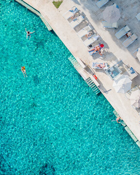 Aerial view of turquoise waters contrast with the sun-kissed patio where figures recline on loungers, Saturnia, Tuscany, Italy.