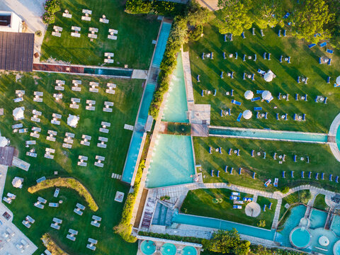 Aerial view of the sun-drenched green lawns and turquoise pools creating a geometric pattern, dotted with sunbeds and umbrellas, Saturnia, Tuscany, Italy.