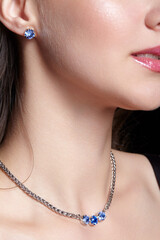 Bijouterie on young female . Woman wears a chainlet with blue rhinestones and earrings.