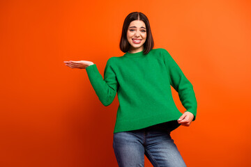 Young stylish woman in a green sweater poses happily against orange background for fashion lifestyle stock photo and advertising campaigns
