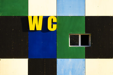 View of a geometric facade with squares of blue, green, black, and white, punctuated by a small window and the bold yellow letters 'WC', Aktau, Mangystau Region, Kazakhstan.