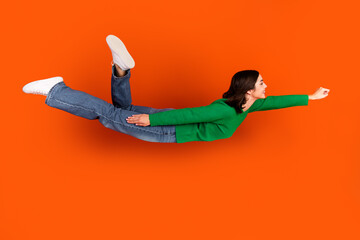Young chic woman in green sweater flies through bright orange background promoting fashion lifestyle and fitness © deagreez