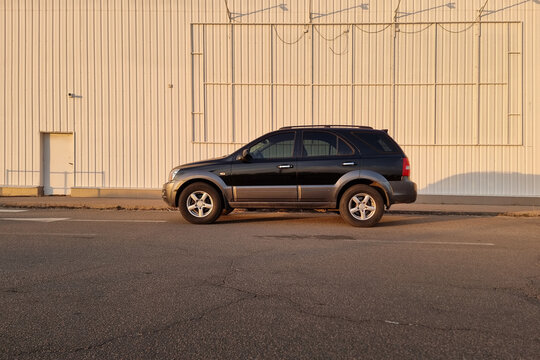 black SUV on the street in industrial district at sunset. Wide angle side profile view of KIA Sorento parked in a city near white wall of a modern building. Kyiv, Ukraine - March 09 2025