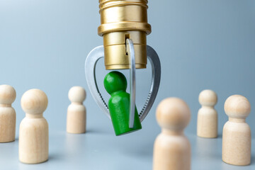 A green wooden figure being chosen by a mechanical claw among other figures. Hiring, human resources, leadership, recruitment and talent selection concept.
