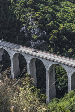 View of an old stone bridge stretching across a lush, green valley, the road surface gleaming in the sunlight, Eze, Provence-Alpes-Cote d'Azur, France.