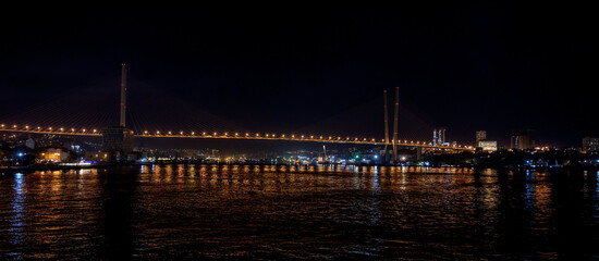 Modern Cable-Stayed Bridge at Night with City Lights and Water Reflection.