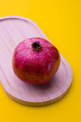 Fresh pomegranate placed on a wooden board against a bright yellow background during daytime