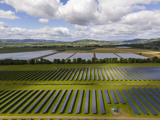 Aerial view of vast solar panel arrays stretch across the verdant landscape, harnessing the sun's energy under a sky dotted with fluffy clouds, Perth, Scotland, United Kingdom.