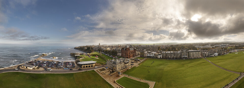 Aerial view of a coastal town with bright green fields contrasting with the dark ocean and cloudy skies, St Andrews, Scotland, United Kingdom.