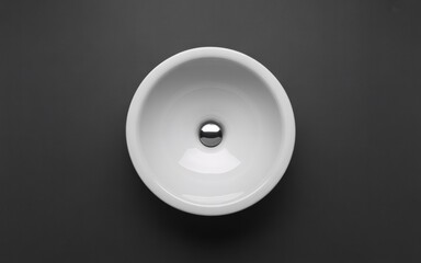 Modern white ceramic washbasin with chrome drain plug on dark background
