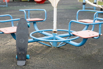 Lonely skateboard propped against empty carousel with no children around, illustrating forgotten toy, absence, and social campaign materials about screen time versus outdoor play