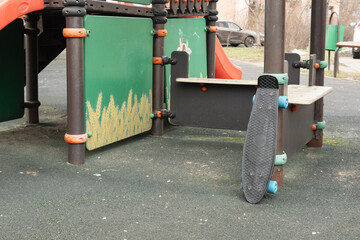 Small skateboard leaning against colorful playground structure on rubber surface, symbolizing outdoor play, kids physical activity, and urban family lifestyle or sport education content