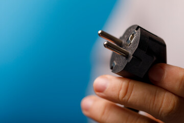 Close-up of a hand holding an EU type electrical plug against a blue background, perfect for energy, power, an